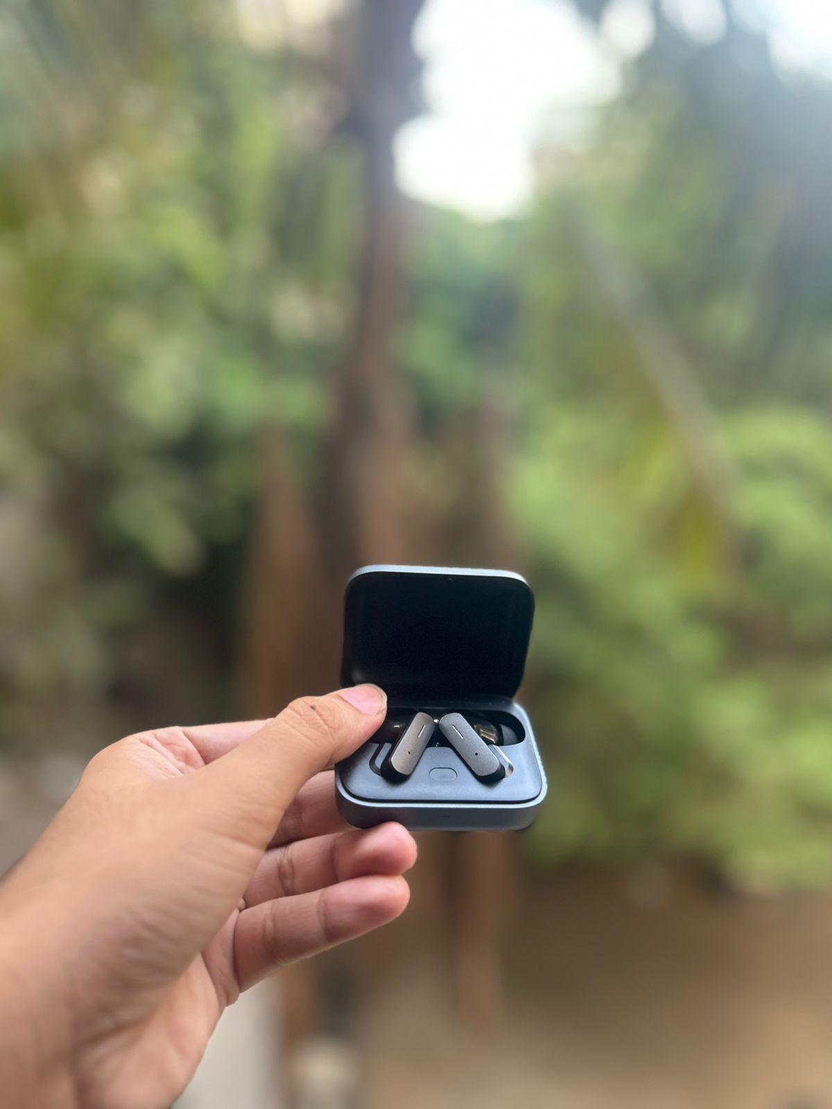 Buds Pro 9 Graphite Dark earbuds held in hand outdoors